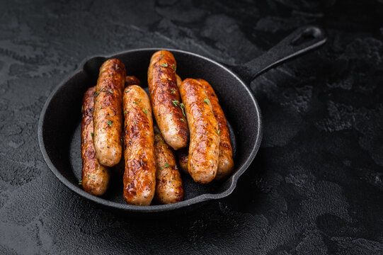 Fried sausage links in black cast iron pan. Golden browned pork sausages on dark rustic background perfect for meal serving.