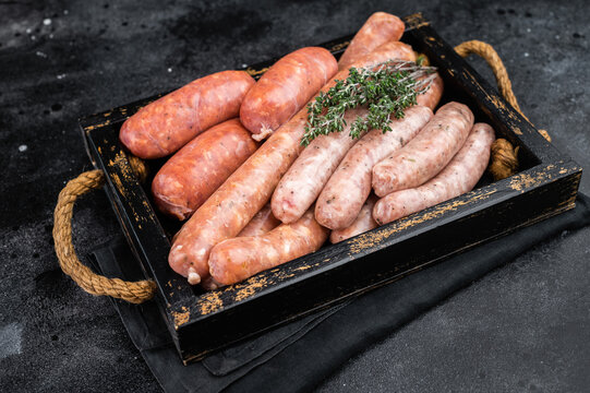 Mix of raw pork sausages in wooden tray with herbs