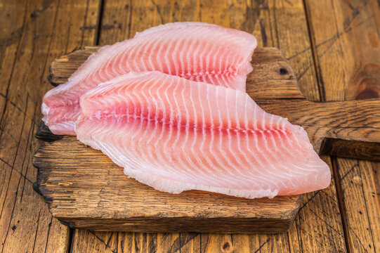 Raw tilapia fish fillets with garlic and herbs on rustic wooden cutting board, fresh white fish seafood.