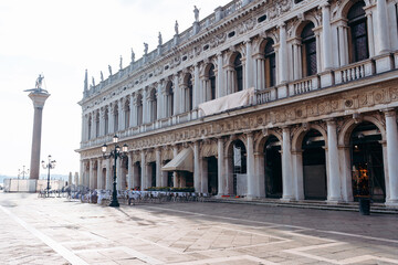 Fototapeta premium Visitors explore St. Mark's Square in Venice with buildings and a column in view