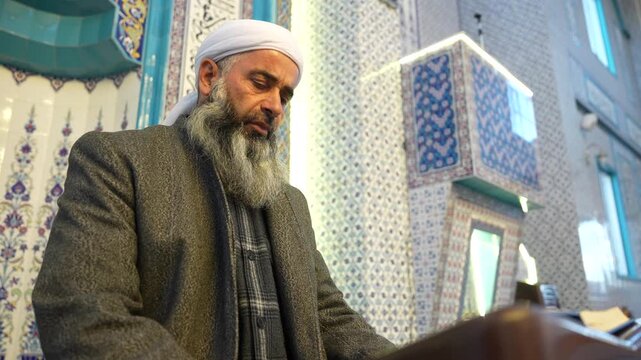 A Muslim sheikh reading the Qur&rsquo;an in the mihrab of the mosque, an elderly Muslim man praying during Ramadan. Concept of religions, Eid al-Fitr.