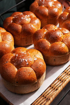 Baker Holding Tray of Fresh Brioche Buns with Sea Salt. A person holds a tray with golden brown, flower shaped brioche buns topped with sea salt, fresh from a professional bakery or restaurant kitchen