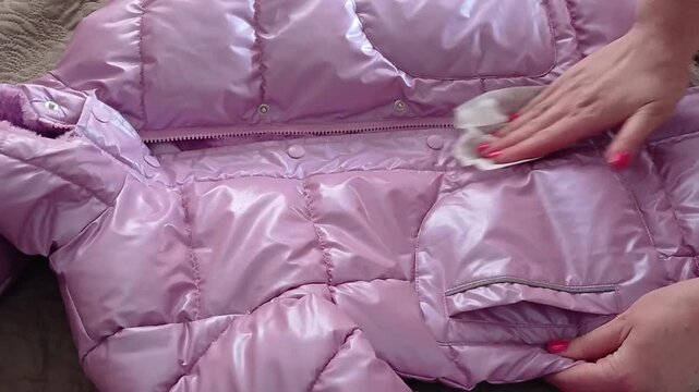 Stock video of how to wet wipe a winter purple warm children's jacket with a damp cloth