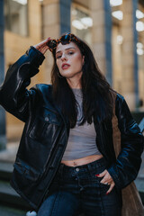 Girl with long dark hair wearing a black leather jacket and sunglasses. She poses confidently...