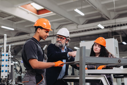 Experienced engineer guiding young manufacturing apprentices in factory