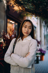 Portrait of serious Asian woman with arms crossed in front of flower shop. Symbolizes calm...