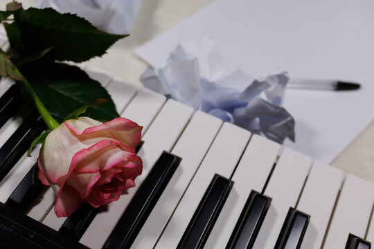 Piano keys with rose and crumpled lyric sheets representing songwriting process. Creative inspiration, composing romantic music and artistic struggle behind melody creation
