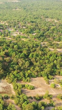 Drone shot of lush green forest and scattered rural houses near Banteay Samre, Cambodia. Natural landscape with trees and open clearings in the countryside.