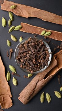 Top View of Cloves (Laung) in White Bowl with Cinnamon Sticks (Dalchini) and Cardamom (Elechi) on Black Background &ndash; Rotating Footage