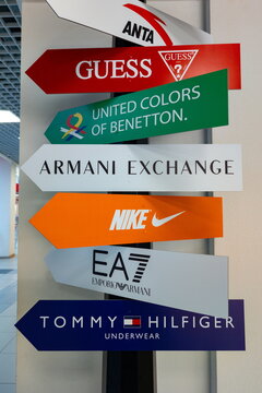 Signs showing brand names like Guess, Nike, Tommy Hilfiger, and Armani Exchange in a shopping mall during daytime