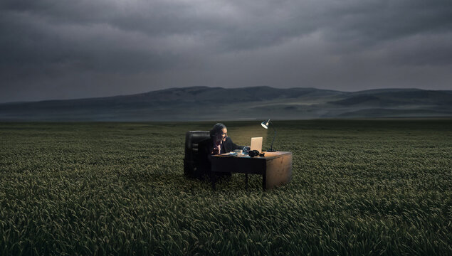 Businesswoman working at desk with laptop in vast green field under cloudy sky, cinematic metaphor of independence, focus and escaping office routine for advertising, corporate storytelling.