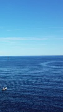 Wide view of a small boat and distant sailboat on the tranquil blue waters near Capo Palinuro, Italy under a clear sky.