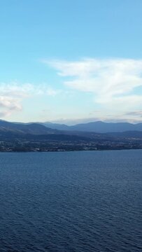 Serene view of calm blue sea with distant mountains and a coastal town near Patras, Greece under a clear sky.