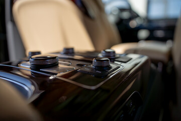 Rear seat center console with multimedia control knobs and buttons on wood trim panel in luxury car interior.