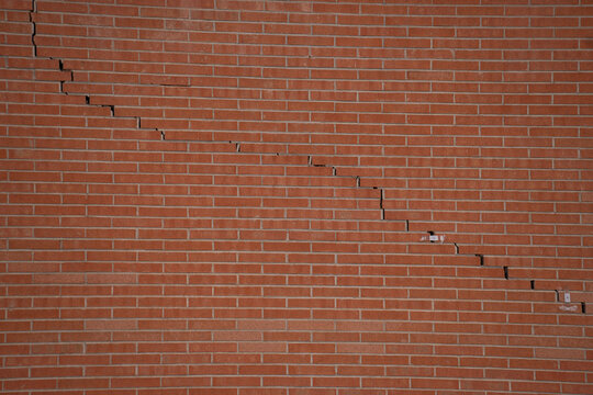 red brick wall with a diagonal crack in the brick horizontal architectural construction masonwork background backdrop with fault line going through middle 