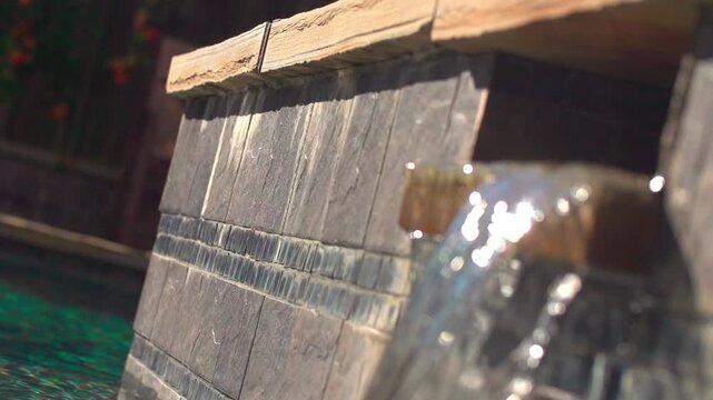 A selective focus slow-motion of a pool wall with a blurred foreground of a small scupper waterfall