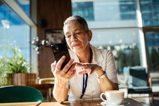 Senior woman using smartphone in modern cafe during coffee break
