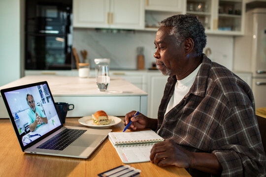 Senior man having online doctor consultation in home kitchen