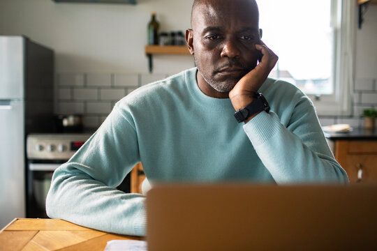 Concerned man working on laptop in home kitchen