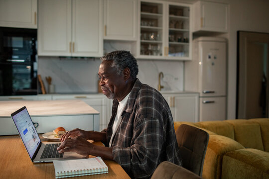 Senior man using laptop at home kitchen