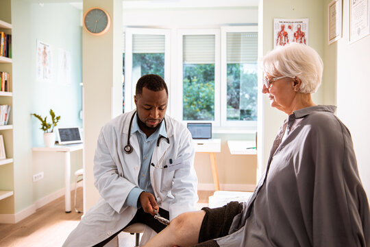 Doctor testing knee reflex of senior patient in clinic
