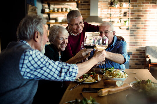 Senior friends toasting wine at dinner in cozy home kitchen