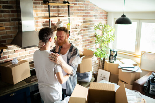Two men embrace amid moving boxes in new home kitchen