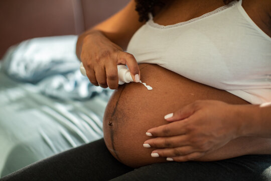 Pregnant woman applying belly lotion at home