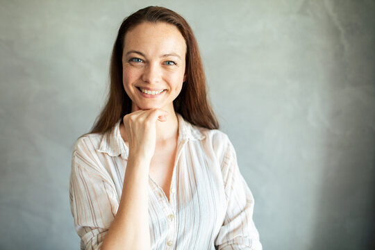 Smiling young woman posing indoors with hand on chin