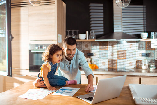 Father and daughter reviewing bills on laptop in home kitchen