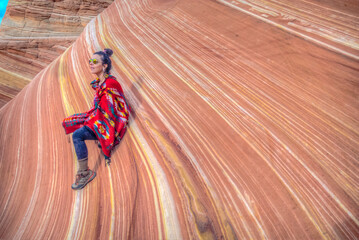 A woman is sitting on a rock with a red blanket draped over her © ExploringandLiving