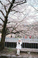 Fototapeta premium Young woman cherry blossom spring tree outdoor sitting white dress boots nature park smiling flower season leisure casual female beauty happiness sunlight peaceful fresh bloom petals trunk grass