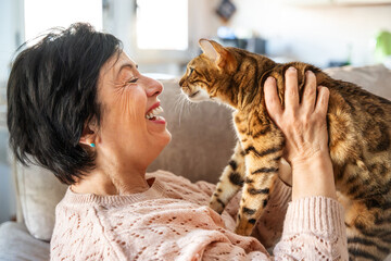 Old woman having fun with her cat sitting on the couch at home - Smiling kitty owner playing in the living room - Animal and people life style concept © Davide Angelini