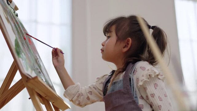 Asian girl focusing while painting on canvas at home