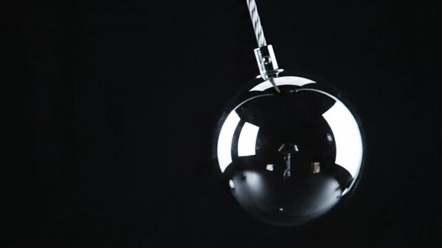 Shiny chrome ball pendulum swinging against a black background with reflections and ambient lighting