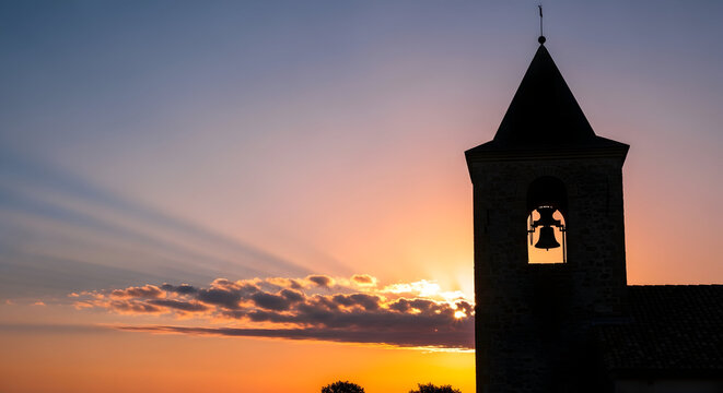 A serene church tower at sunset with a bell and a picturesque sky