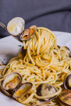 Spaghetti con sugo di vongole, aglio e prezzemolo servito come primo piatto in un ristorante elegante con un cliente che li arrotola su una forchetta
