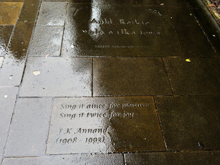 Obraz premium Wet stone pavement with engraved inscriptions and J. K. Annand poetry on a rainy day in Edinburgh, Scotland, UK