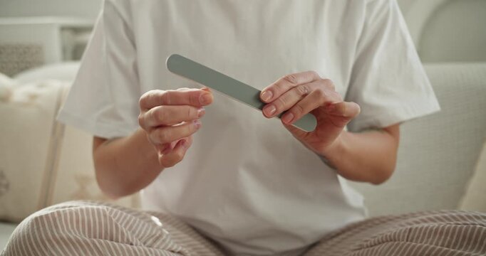 Woman filing her nails with an emery board during her morning beauty routine at home