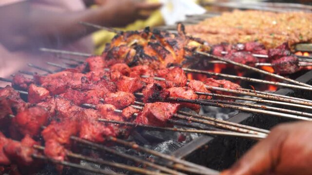 Indian chef cooking barbecue skewers on grill at street stall