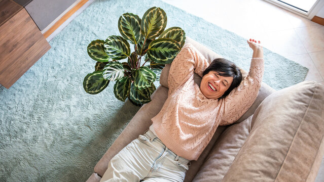 Happy senior woman relaxing on the sofa at home - Smiling female pensioner enjoying day off lying on the couch - Healthy life style, good vibes people and pension concept