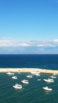 Small fishing boats anchored in the tranquil harbor of Koroni, Greece, with a clear blue sea and distant mountains under a bright sky.