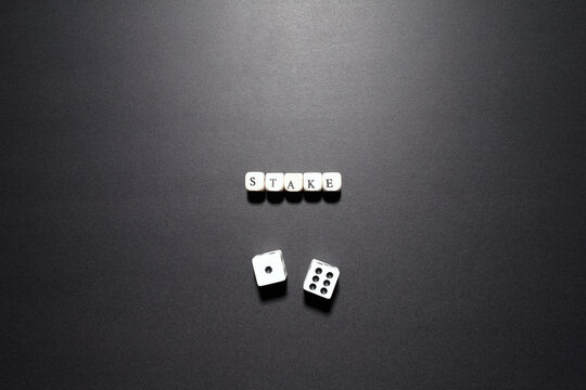Stake word above dice representing financial exposure, risk position, and betting capital.