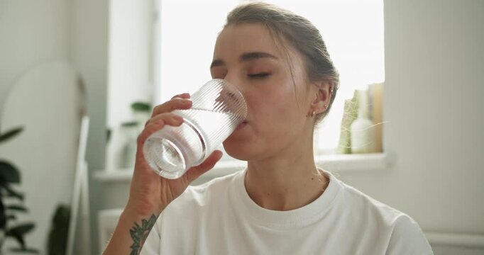 Young woman drinking water for hydration and wellness in a bright living room