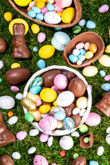 Easter egg hunting background with chocolate eggs. Various candy and chocolate Easter eggs, bunny and rabbits with basket for eggs on green grass park or garden background
