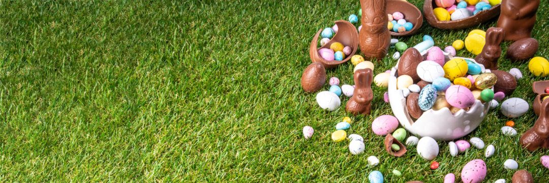 Easter egg hunting background with chocolate eggs. Various candy and chocolate Easter eggs, bunny and rabbits with basket for eggs on green grass park or garden background