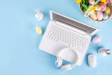 Easter office workplace, preparation for holiday, spring Easter sale, blogging. White laptop keyboard with easter eggs basket and flower branch decorations, on light blue wooden table top view 