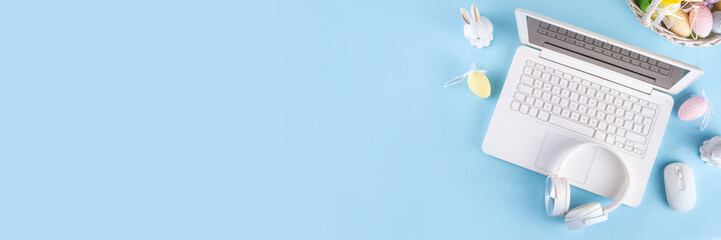 Obraz premium Easter office workplace, preparation for holiday, spring Easter sale, blogging. White laptop keyboard with easter eggs basket and flower branch decorations, on light blue wooden table top view 