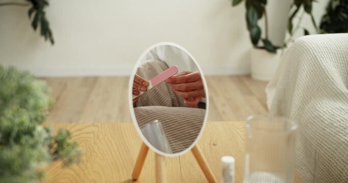 Woman's reflection filing nails with emery board for home manicure routine