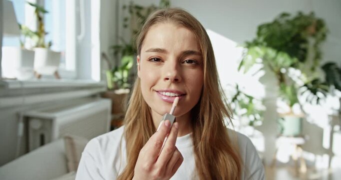 Beautiful smiling woman applying lip gloss during her morning beauty routine at home